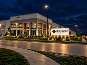 Illuminated Blue Ridge Commerce Center cabinet sign glowing white at night on a landscaped base in front of a tilt-wall industrial building with a lit glass entrance